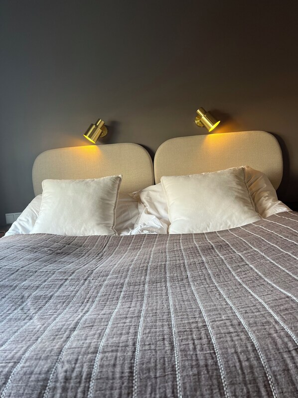 A bed with a textured gray blanket, two pillows, and two wall-mounted lamps.