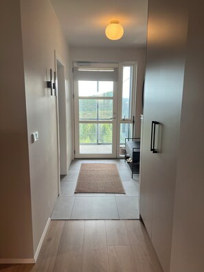 A hallway with a door leading to a balcony, a rug on the floor, and a ceiling light. - Modern & cozy apartment in Capital area - scenic views in nature! (Garðabær)