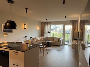A modern living room with a sofa, dining table, and kitchen area. - Modern & cozy apartment in Capital area - scenic views in nature! (Garðabær)