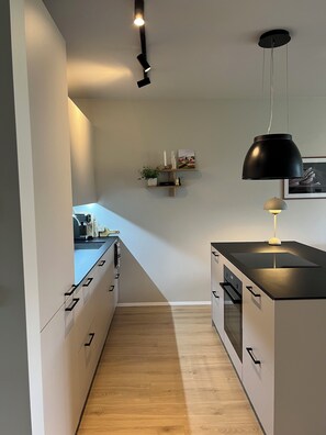 A modern kitchen with a central island, wooden flooring, and pendant lighting.