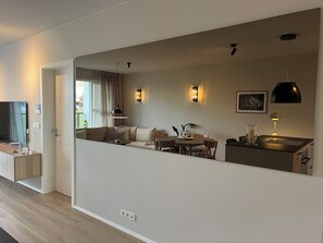 Un saló modern amb un sofà, taula de dinar i cadires, un televisor i un mirall gran que reflecteix l'espai.