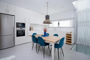 A modern kitchen with white cabinets, a wooden dining table, blue chairs, and a hanging pendant light. - Fahana Canteras (LAS PALMAS DE GRAN CANARIA)