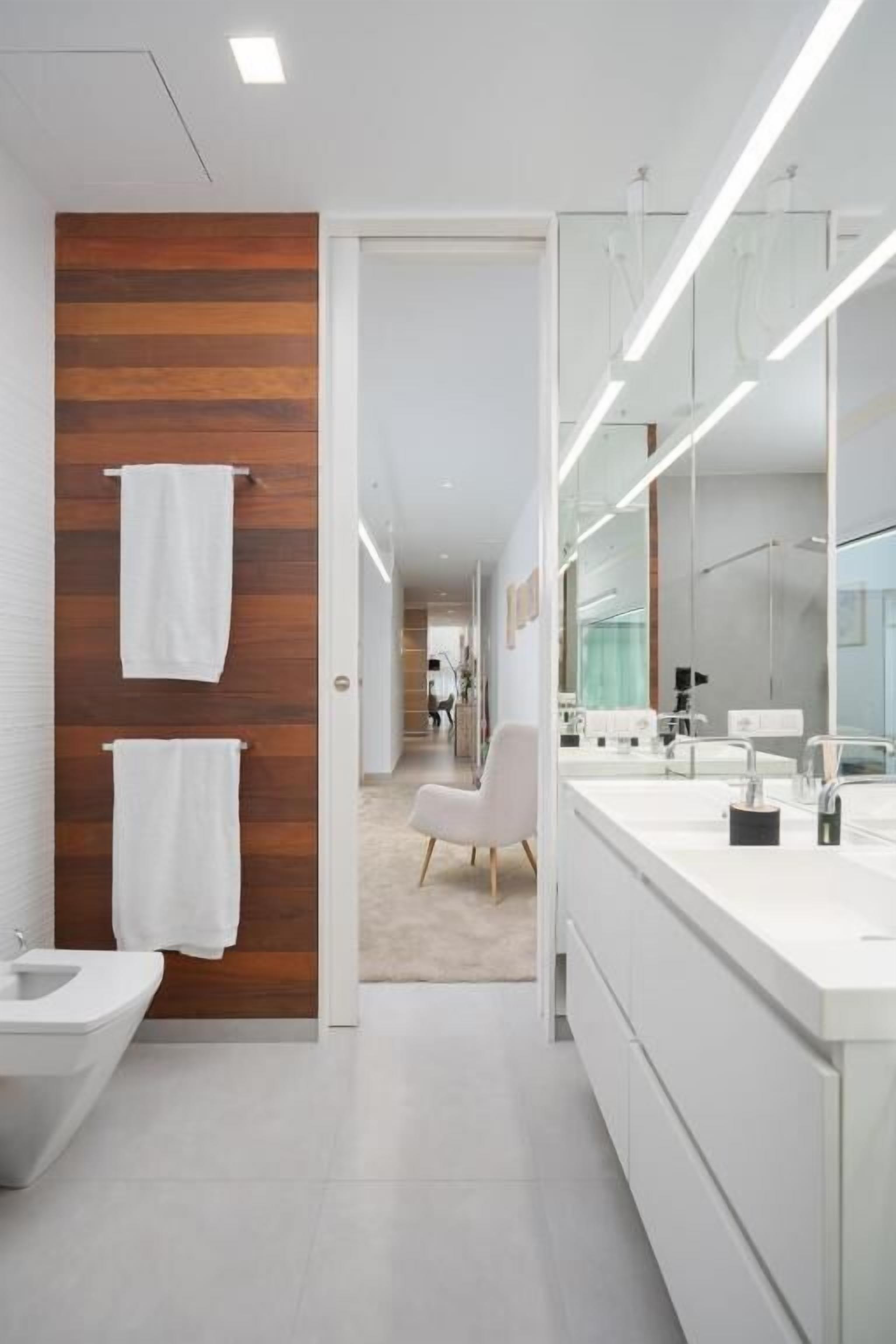 A modern bathroom with a wooden accent wall, a white sink, and a large mirror.