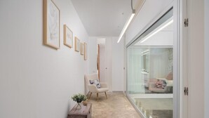 A hallway with framed artwork on the wall, a chair, a small table with a plant, and a sliding glass door leading to a bedroom. - Fahana Canteras (LAS PALMAS DE GRAN CANARIA)