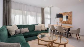 A modern living room with a green sofa, a glass coffee table, and a dining area with chairs and a table.