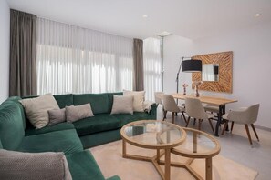 Ein modernes Wohnzimmer mit einem grünen Sofa, einem Glastisch und einem Essbereich mit Stühlen und einem Tisch.