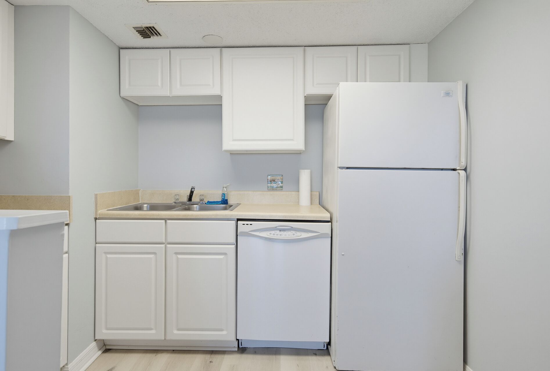 A kitchen with white cabinets, a sink, a dishwasher, and a refrigerator.