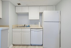 Una cocina con gabinetes blancos, un fregadero, lavavajillas y refrigerador.