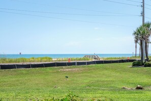 A grassy area with a view of the ocean, a wooden structure, and a utility pole. - Oceanfront 2BR/2BA Condo - Pool + Beach - Ormond-by-the-Sea (Ormond Beach)