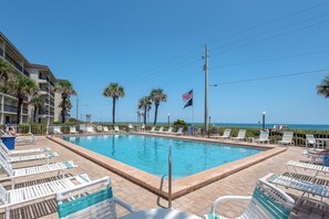 A swimming pool with lounge chairs, a flag, and a view of the ocean. - Oceanfront 2BR/2BA Condo - Pool + Beach - Ormond-by-the-Sea (Ormond Beach)