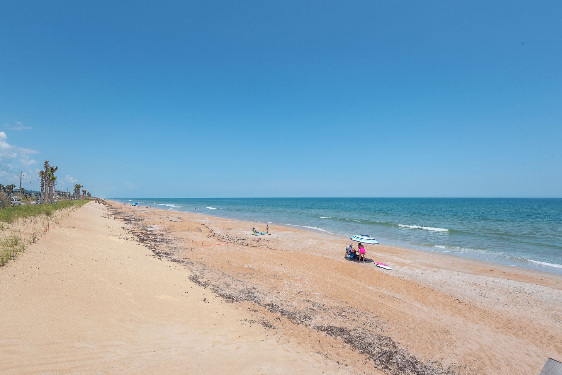 Une plage avec un ciel dégagé, un rivage sablonneux, et quelques personnes et parasols.