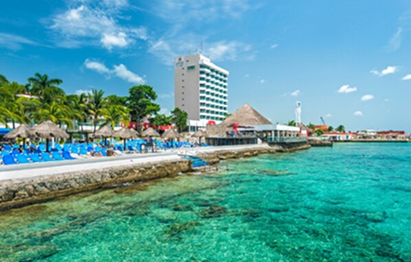 Ein Strandhotel mit Poolbereich, Palmen und blauem Himmel.