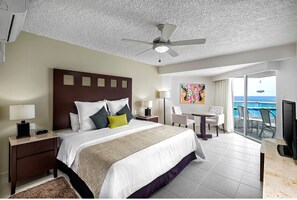 Ein Hotelzimmer mit einem großen Bett, einem Deckenventilator, einem Schreibtisch mit Stuhl, einem Fernseher und einem Balkon mit Meerblick.