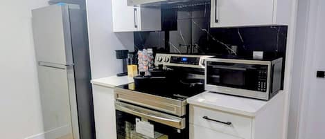 A modern kitchen with white cabinets, stainless steel appliances, and a wooden floor.