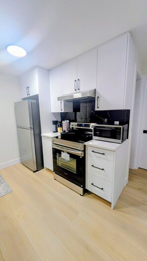 A modern kitchen with white cabinets, stainless steel appliances, and a wooden floor. - Sweet Home Escape 2BR Guest Suite (Edmonton)