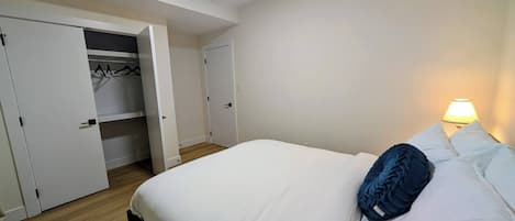A hotel room with a bed, a bedside lamp, and a wardrobe with hanging clothes.