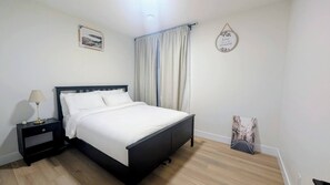 Un dormitorio con cama, mesita de noche, lámpara, ventana con cortinas y adornos en la pared.