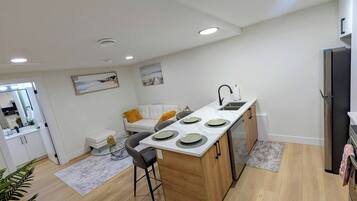 A modern kitchen with a central island, white cabinetry, and a dining area with a white sofa and a small table.