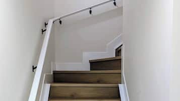 Una escalera de madera con paredes blancas y un cuadro de paisaje urbano.