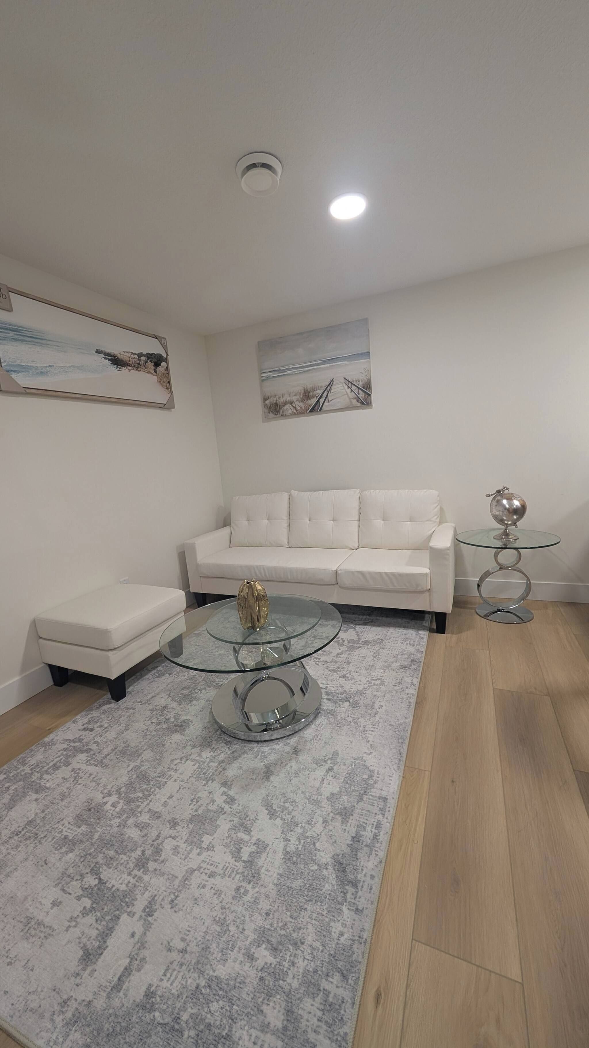 A modern living room with a white sofa, a glass coffee table, and a patterned rug.