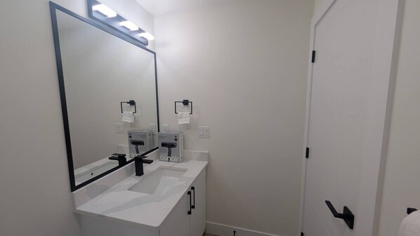 A bathroom with a white sink, a large mirror, and a door with a black handle.