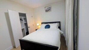 Un dormitorio con cama, mesita de noche, lámpara, armario y un cuadro en la pared.