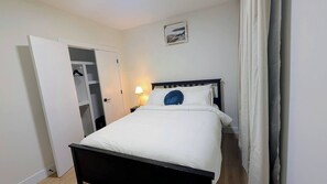 A bedroom with a bed, a nightstand, a lamp, a wardrobe, and a picture on the wall.