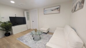 Una sala de estar moderna con un sofá blanco, una mesa de centro de vidrio, un televisor de pantalla plana y un cuadro en la pared.