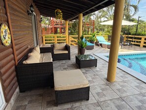 A covered outdoor seating area with wicker furniture and a pool.