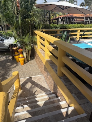 A yellow railing, a pool, and outdoor seating with umbrellas.