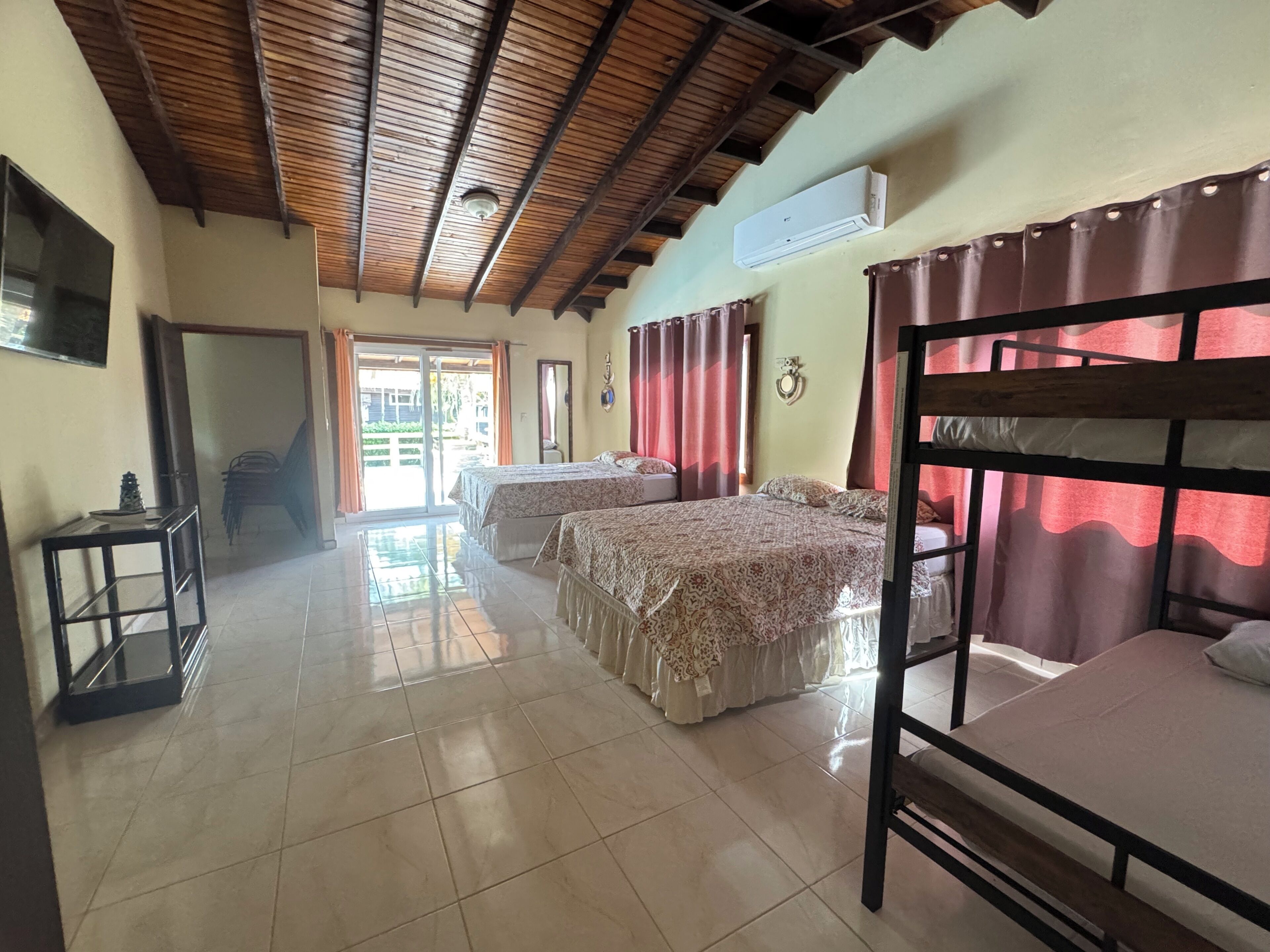 A room with two beds, a TV, and a sliding door leading to an outdoor area.