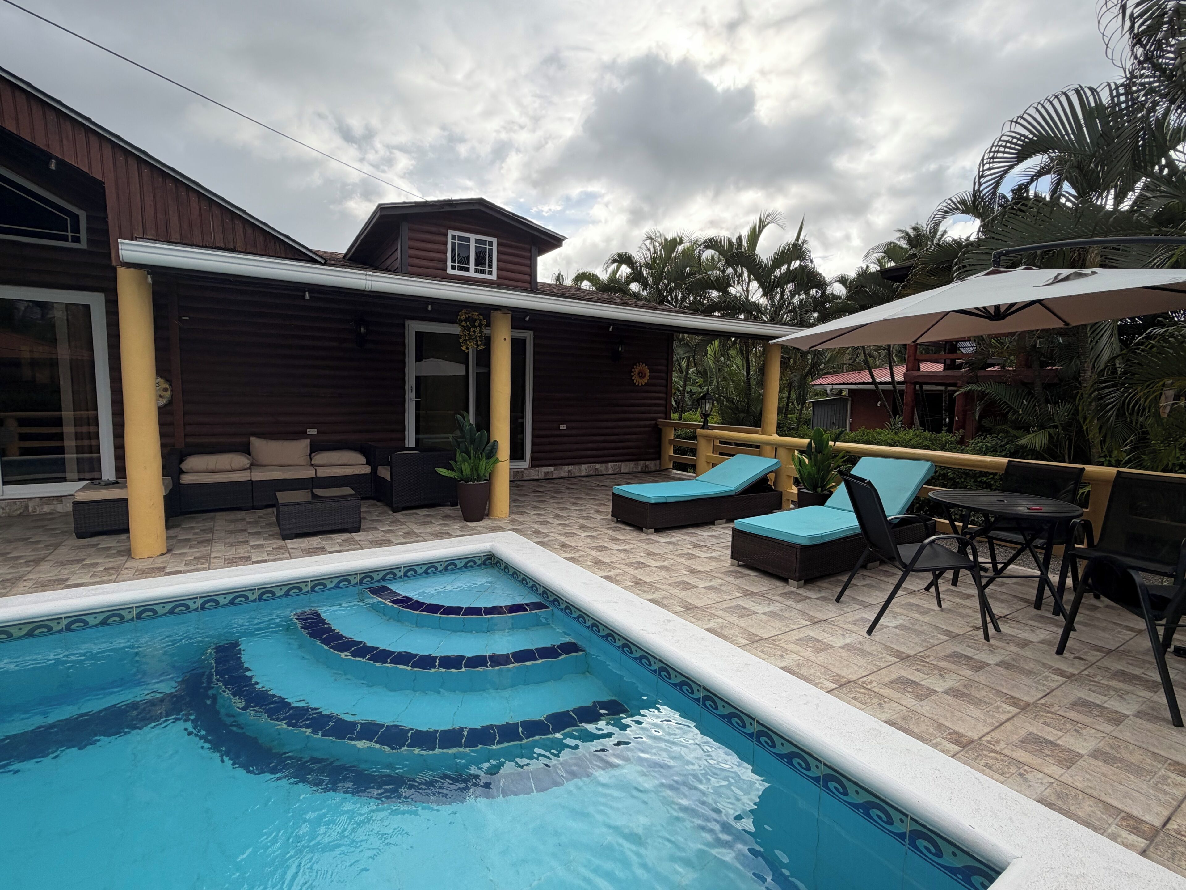 A swimming pool with tiered steps, outdoor seating, and a covered patio area.