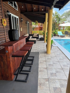 A covered outdoor seating area with a pool in the background.