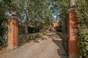 A gated entrance to a property with a gravel path leading to a red door, surrounded by trimmed hedges and trees. - Wilde Cedar with swimming pool (Binfield)