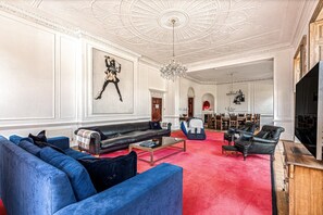 A spacious living room with a red carpet, a black leather sofa, a blue armchair, and a chandelier. - Wilde Cedar with swimming pool (Binfield)