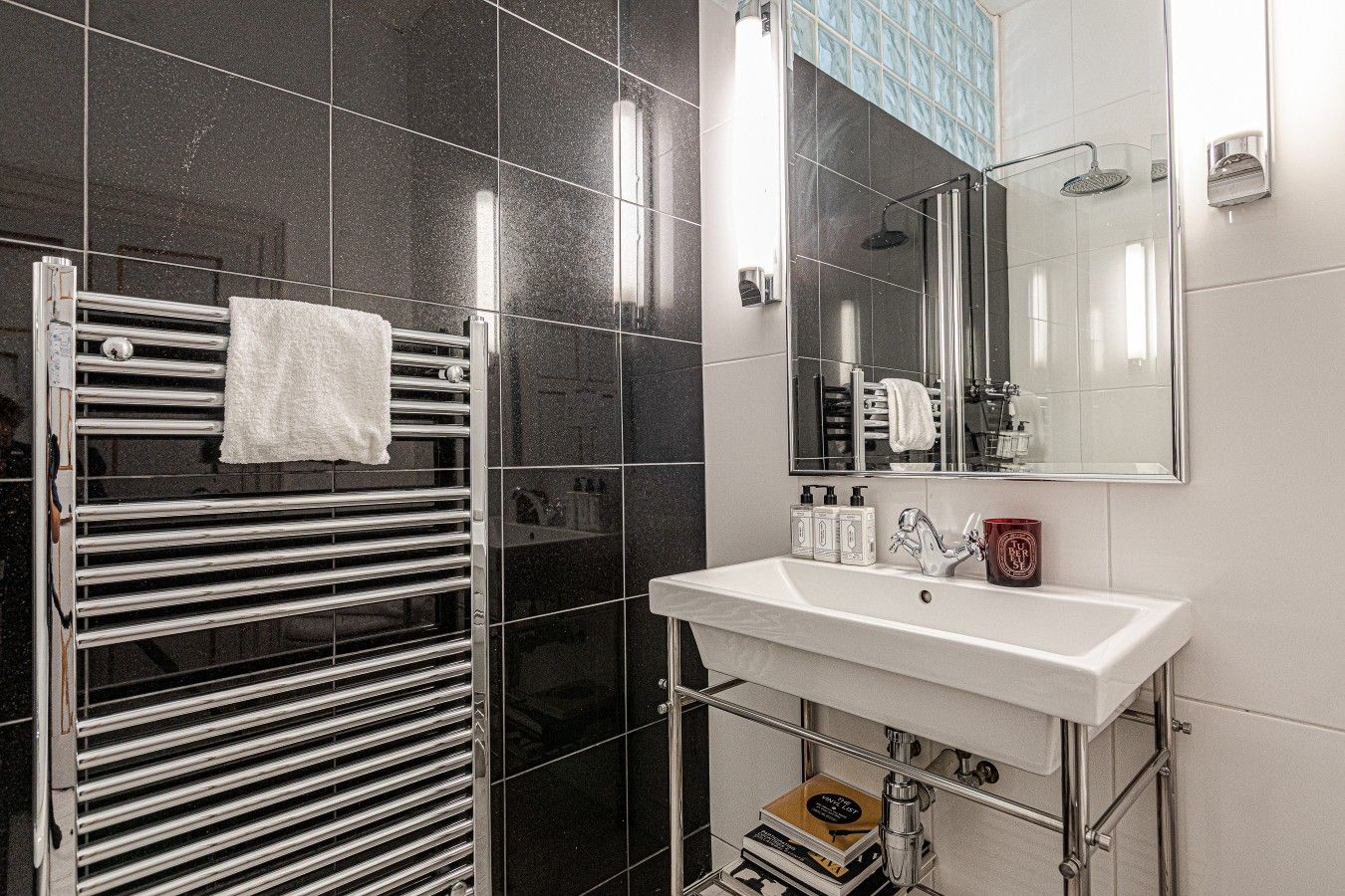 A modern bathroom with a glass shower enclosure, a white sink with a mirror above, and a towel rack with a white towel.