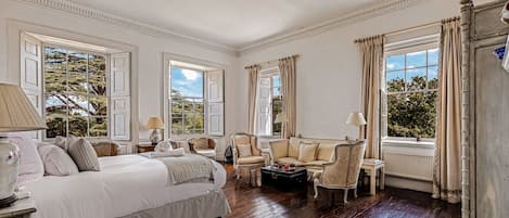 A classic room with a large bed, two armchairs, a small table, and a window with curtains.
