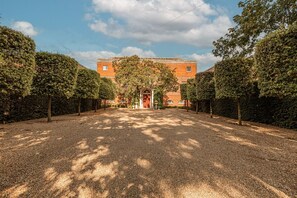A gravel driveway leading to a building with a red door, surrounded by trees and hedges. - Wilde Cedar with swimming pool (Binfield)