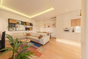 A modern living room with a sofa, coffee table, and a dining area. There is a kitchen with cabinets and an oven. - ‘Almaroma Central’ Apartment with Private Terrace, Wi-Fi & Air Conditioning (Seville)