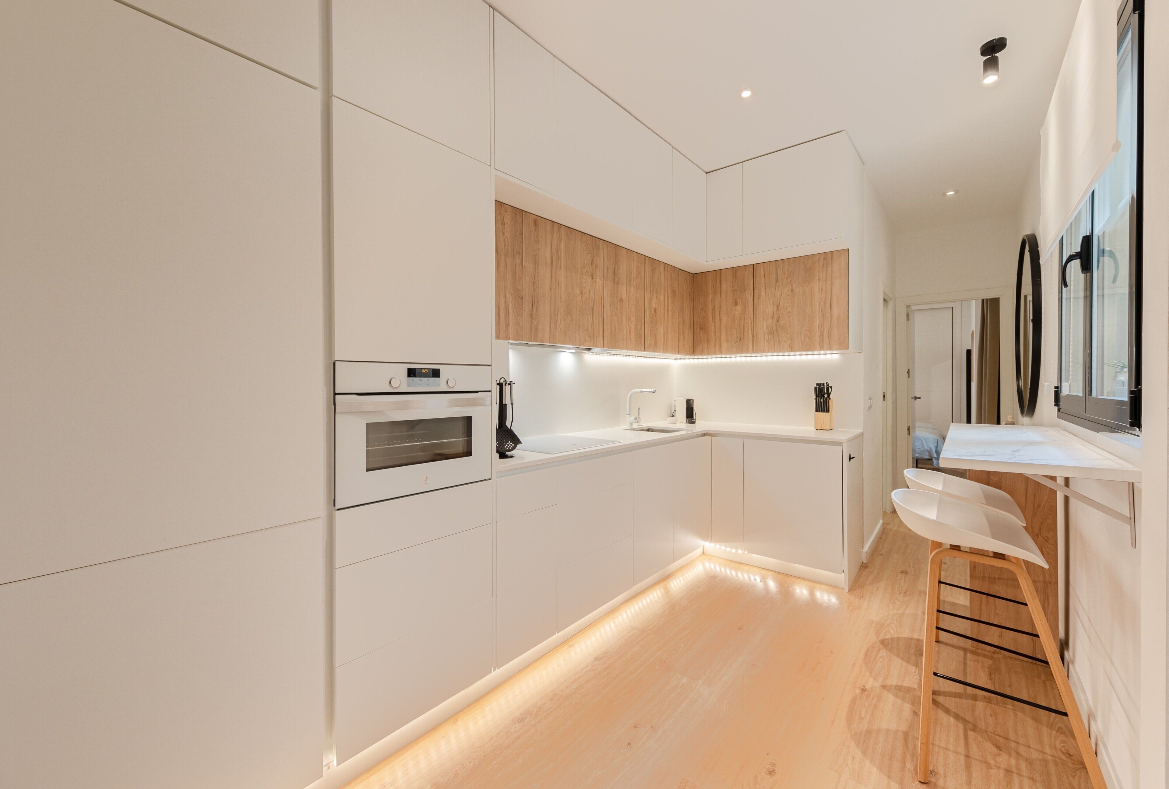 Una cocina moderna con armarios blancos, encimera de madera y horno empotrado.