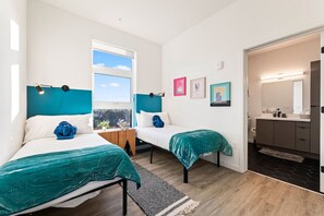 Ein modernes Schlafzimmer mit zwei Betten, einem Fenster und einem durchgegangenen Tür erkennbaren Badezimmer.