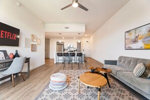 A modern living room with a sofa, a coffee table, a TV, and a kitchen in the background. - Private Skyloft W/ DTLA Views - 1Mi to  Dodger Std (Los Angeles)