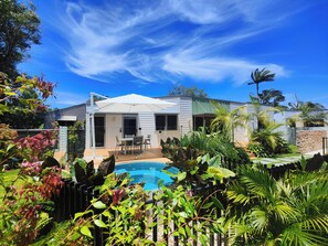 Una propiedad residencial con piscina, mobiliario de patio y exuberante vegetación.