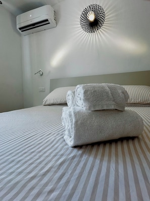 A hotel room with a bed, striped bedding, a wall-mounted air conditioner, and a decorative light fixture. - Stella Marina. Your getaway just a stone's throw from the sea, Ligurian villages, and the French Riviera. (Bordighera)