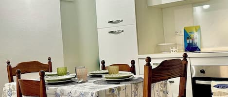 A dining area with a round table, four wooden chairs, and a patterned tablecloth.