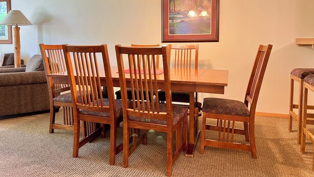 A dining area with a wooden table and chairs, a painting on the wall, and a lamp. - Meadow Lake Private Timeshares (Columbia Falls)