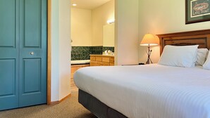 A hotel room with a bed, a nightstand, a lamp, a bathroom with a mirror, and a door. - Meadow Lake Private Timeshares (Columbia Falls)