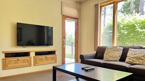 A living room with a flat-screen TV mounted on the wall, a sofa with patterned cushions, a coffee table, and a sliding glass door leading to an outdoor area. - Meadow Lake Private Timeshares (Columbia Falls)