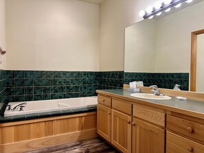Une salle de bain avec une baignoire, deux lavabos, des meubles en bois et un grand miroir.