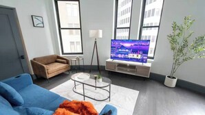 A modern living room with a blue sofa, a coffee table, a television, and a potted plant. - Urban 1BR Downtown–Close (Pittsburgh)